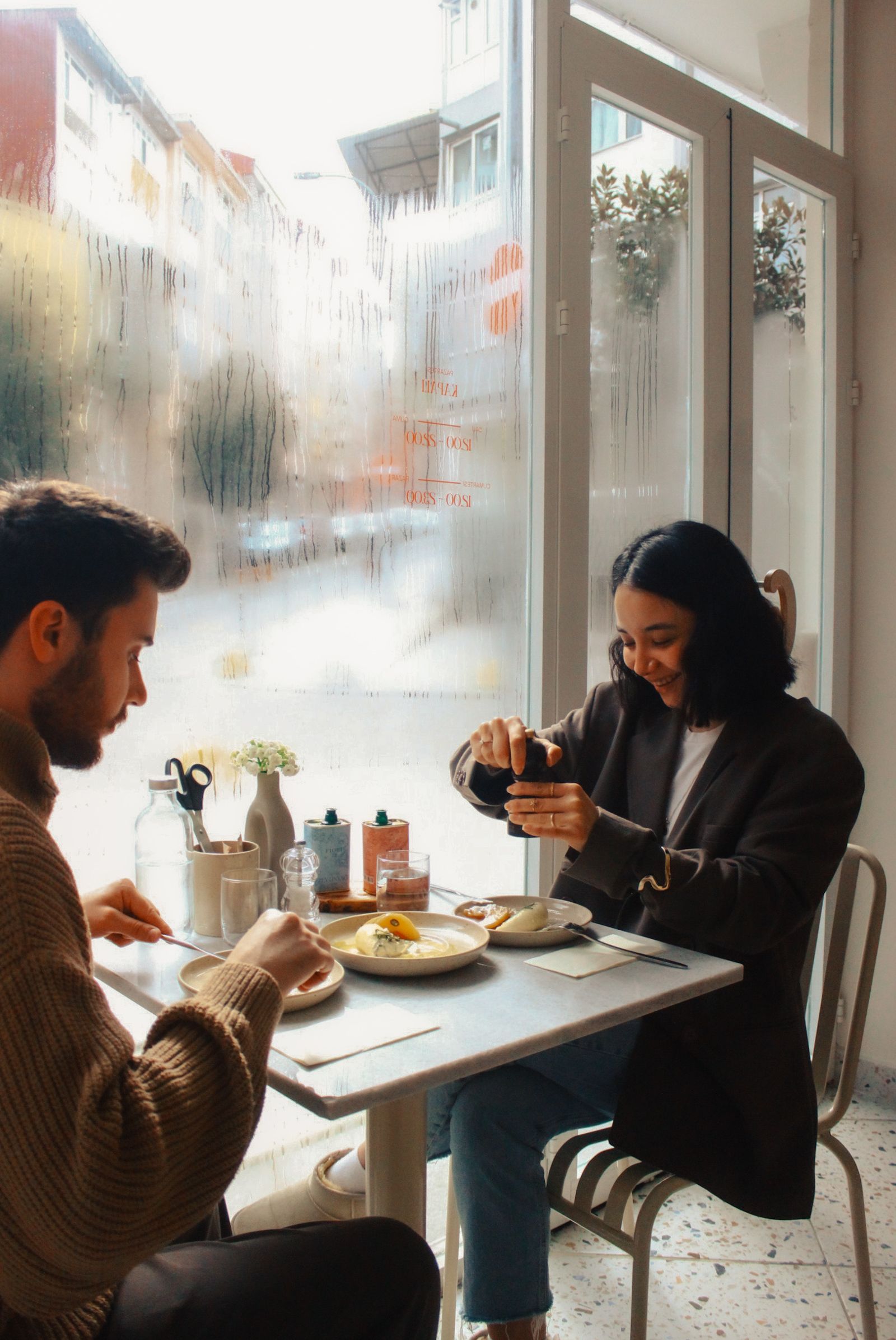 Zwei Gäste an einem beschlagenen Caféfenster bei Regen