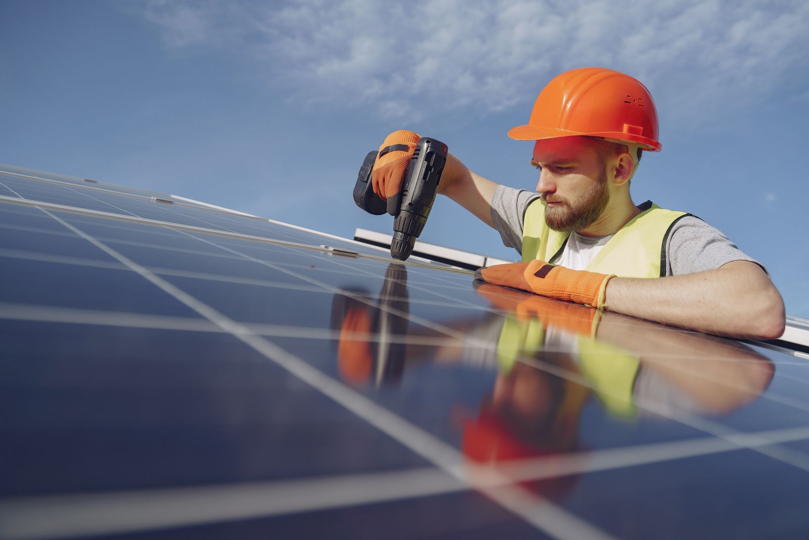 Monteur montiert ein Photovoltaikmodul vor blauem Himmel